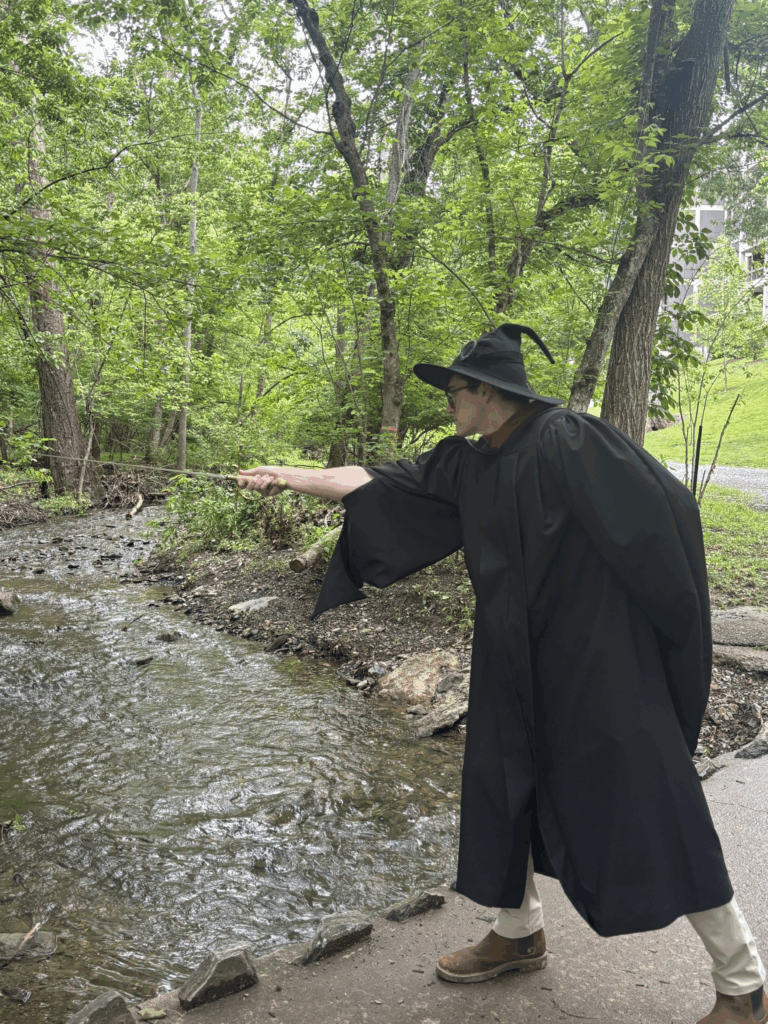 Man in black cloak and wizard hat pointing sword at creek